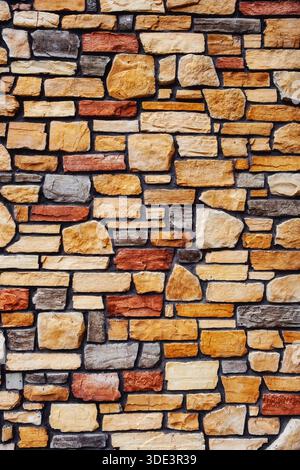 Eine rustikale Steinmauer mit einem unregelmäßigen, mehrfarbigen Muster aus annähernd rechteckigen und unregelmäßig geformten Steinen in Beige-, Braun-, Grau-, Stockfoto