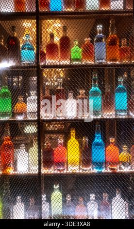Farbenfrohe Spirituosenflaschen auf beleuchteten Barregalen mit Neonlichtern hinter einem abgeschirmten Fenster Stockfoto
