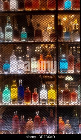 Farbenfrohe Spirituosenflaschen auf beleuchteten Barregalen mit Neonlichtern hinter einem abgeschirmten Fenster Stockfoto