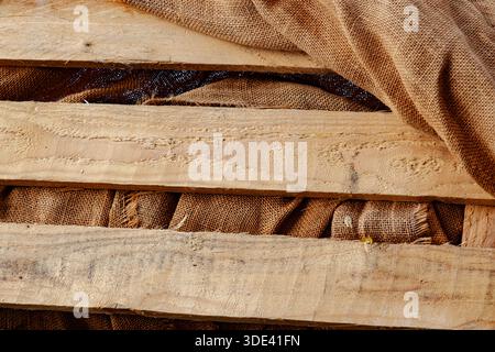 Strukturierter brauner Sackleinen-Stoff, der über einer verwitterten, beigen Holzleiste hängt Stockfoto