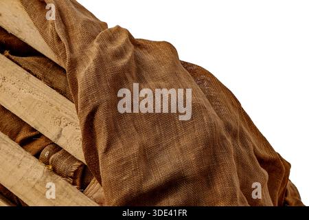 Strukturierter brauner Sackleinen-Stoff, der über einer verwitterten, beigen Holzleiste hängt Stockfoto