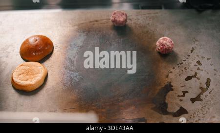 Rohe Burger-Fleischbällchen und Brioche-Brötchen auf einem heißen, kommerziellen Grill Stockfoto