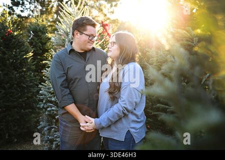 Ein Paar hält Hände und lächelt im leuchtenden Weihnachtsbaumlicht Stockfoto