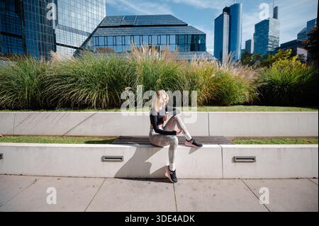 Mädchen in Sportbekleidung sitzt auf der Bank im modernen Stadtpark Stockfoto