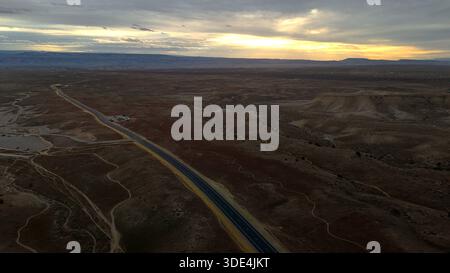 Eine lange, gerade Straße aus der Vogelperspektive führt durch die trockene Landschaft unter einem Himmel, der mit dem schwindenden Glanz des Sonnenuntergangs in Fruita, Colorado, Vereinigte Staaten Stockfoto