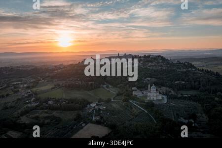 Aus der Vogelperspektive des goldenen Sonnenlichts, das die alte Architektur auf den grünen Hügeln küsst und den Himmel in Orange und Blau malte, Montepulciano, Tu Stockfoto