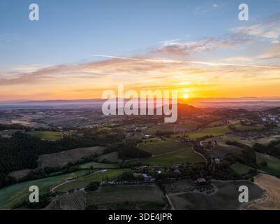 Aus der Vogelperspektive auf die Sonne, die unter dem Horizont taucht und einen warmen Glanz über die sanften Hügel und Weinberge der Toskana, Montepulciano, Toskana, Italien ausstrahlt. Stockfoto