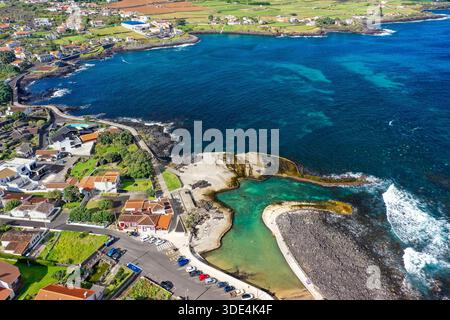 Aus der Vogelperspektive auf die zerklüftete Küste trifft auf das türkisfarbene Wasser in der Nähe des Leuchtturms, eine Symphonie aus Blau und Grün, Porto Martins, Azoren, Portugal. Stockfoto
