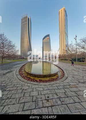 Mailand Italien. Stadtteil CityLife. Drei zeitgenössische Glastürme ragen über einem ruhigen Park mit einem flachen, ovalen Brunnen, der den Himmel und b reflektiert Stockfoto