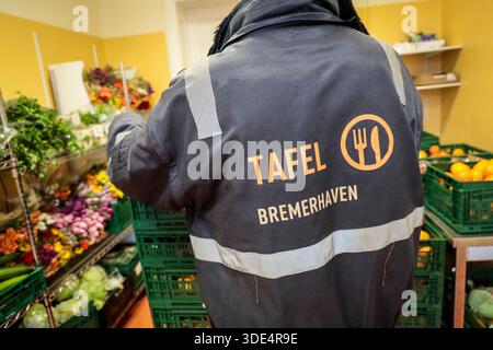 Bremerhaven, Deutschland. Januar 2026. Ein Helfer mit einer Jacke mit dem Tafel Bremerhaven-Logo posiert vor Obst- und Gemüsekörben, bevor er sie an die Kunden weitergibt. Mit einem neuen Förderverein hat die Bremerhavener Lebensmittelbank ihren Betrieb nach mehrwöchiger Schließung wieder aufgenommen. Rund 1.500 armutsgefährdete Menschen im Bremerhavener Raum können wieder Nahrung von der Tafel beziehen. Quelle: Focke Strangmann/dpa/Alamy Live News Stockfoto