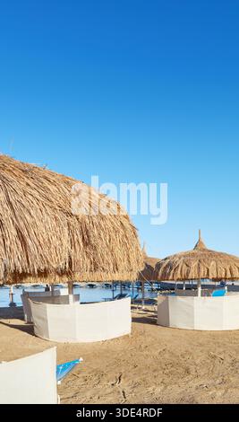 Strohschirme, Sonnenliegen und Windschutzscheiben am Strand in Hurghada, Ägypten. Stockfoto