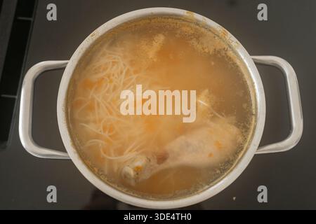 Ein Topf Hühnersuppe, die auf dem Herd kocht, mit Nudeln und Gemüse, die in der Brühe sichtbar sind. Das warme, hausgemachte Gericht vermittelt Komfort und Hausmannskost Stockfoto