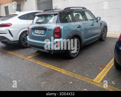 Ein moderner blauer Mini Cooper Countryman parkt an einem bestimmten Ort auf einer nassen Asphaltoberfläche mit gelben Linien Stockfoto