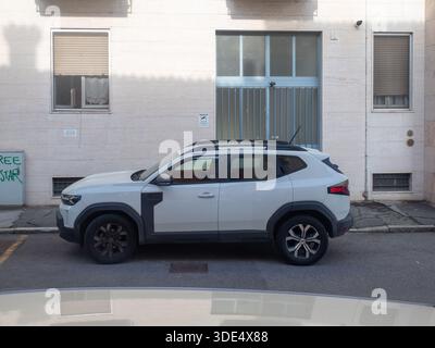 Ein weißer Dacia Duster SUV parkt auf der Straße, von der Seite gesehen, mit einem hellen Gebäude im Hintergrund Stockfoto