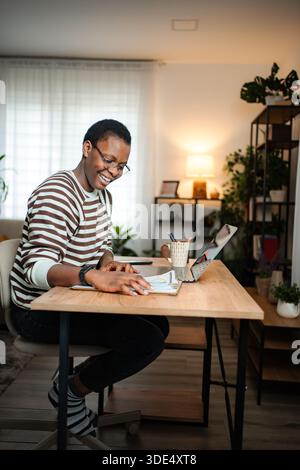 Frau, die von zu Hause aus arbeitet, lächelt beim Lesen von Dokumenten Stockfoto