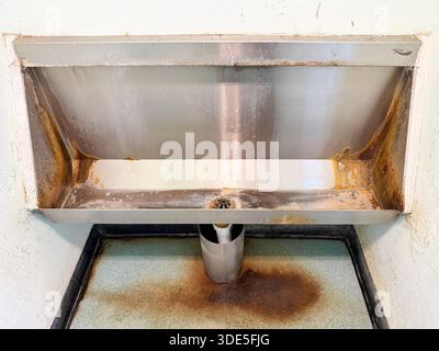 Altes, an der Wand montiertes Edelstahl-Urinal mit sichtbaren Rostflecken und Wasserschäden in einer vernachlässigten öffentlichen Toilette northumberland uk Stockfoto