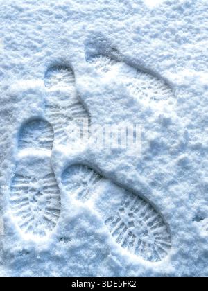 Mehrere Stiefeldrucke in frisch gefallenem Schnee zeigen tiefe Profilmuster und überlappende Schritte auf einem kalten, wintergefrorenen Untergrund Stockfoto