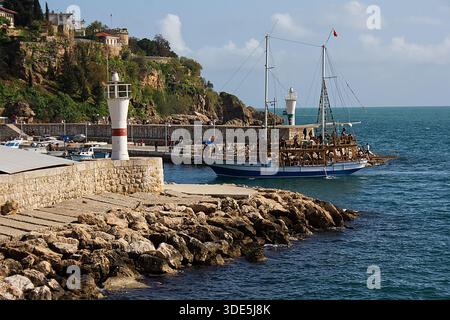 Ein lebhaftes blau-weißes Gulet-Touristenboot mit Passagieren fährt anmutig in den historischen Hafen von Kaleici in Antalya ein Stockfoto
