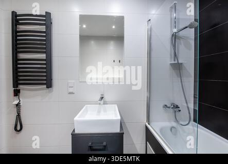 Ein modernes Badezimmer mit schwarzen gefliesten Wänden, Badewanne, Waschbecken und minimalistischen Elementen für ein elegantes und elegantes Aussehen Stockfoto