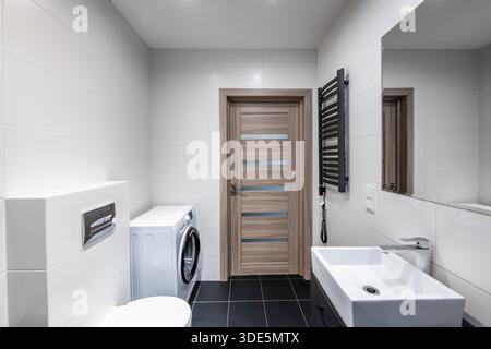 Stilvolles Badezimmer mit Waschmaschine, Holztür und modernen Armaturen, die einen praktischen und eleganten Raum schaffen Stockfoto