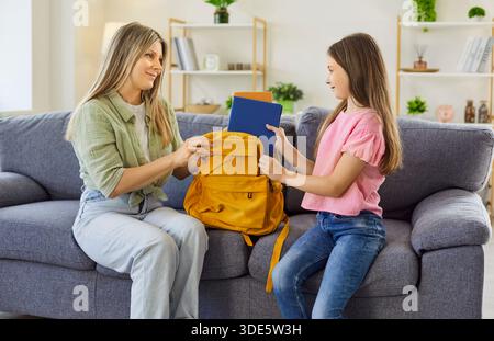 Lächelnde Mutter und Tochter organisieren gemeinsam den Schulrucksack auf der Couch zu Hause Stockfoto
