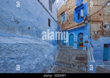 032 schräge und gestufte Straße in der blau lackierten Medina mit drei verzierten Holztüren, mit Nieten und bunt bemalt. Chefchaouen-Marokko. Stockfoto