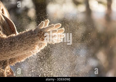 Nahaufnahme von Frauenhänden in weißen Strickhandschuhen, klatschen und schütteln Sie die Hände aus dem Schnee am sonnigen Wintertag Stockfoto