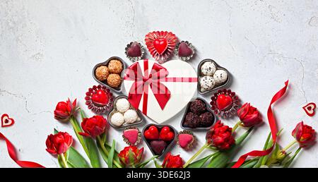 Valentinstag-Geschenkbox mit herzförmiger Schokolade und roten Tulpen auf weiß Stockfoto