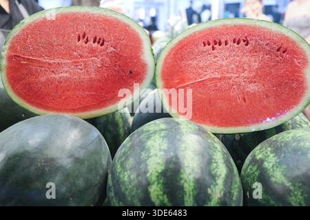 In Scheiben geschnittene Wassermelonenhälften hintereinander auf einem thailändischen Obstmarkt. Leuchtend rotes Fleisch und grüne Rinden für Sommeressen und gesunden Lebensstil. Stockfoto