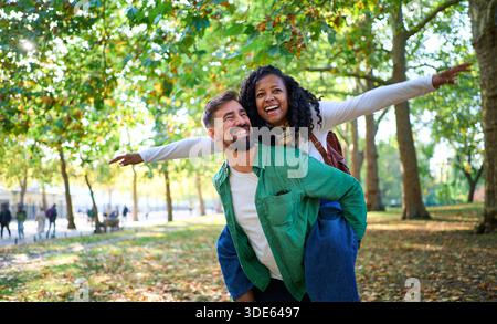 Glückliches junges, vielfältiges Paar, das einen Huckepack-Ritt im Park genießt. Stockfoto