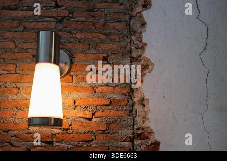 Industrieller Backsteinhintergrund mit moderner Wandleuchte und strukturiertem Putz, bietet Kopierraum für Innenarchitektur und Branding. Stockfoto