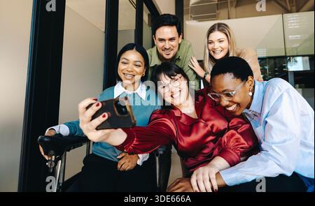 Eine fröhliche Gruppe von Kollegen, die in Alter und Geschlecht unterschiedlich sind, versammelt sich zu einem fröhlichen Selfie in einer modernen Büroumgebung, in der Kameradschaft und ein gezeigt werden Stockfoto
