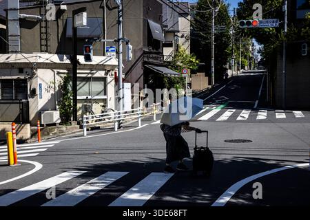 Tokio, Japan - 31. Juli 2025 : Dame überquert die Straße mit einem Regenschirm Stockfoto