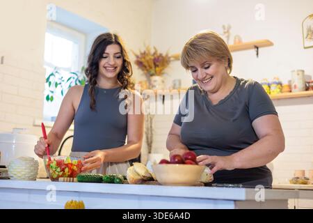Zwei Frauen verschiedener Generationen kochen zusammen in einer gemütlichen Küche. Mutter und Tochter kochen zusammen in einer warmen Küche. Salat zubereiten Stockfoto