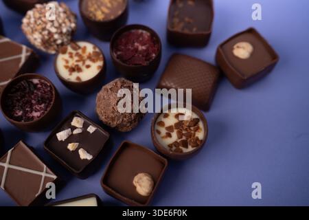 Close-up-Makro mit verschiedenen Gourmet-Pralinen und Trüffeln auf einer violetten Tischplatte mit glänzenden Oberflächen aus dunkler, Milch und weißer Schokolade, t Stockfoto