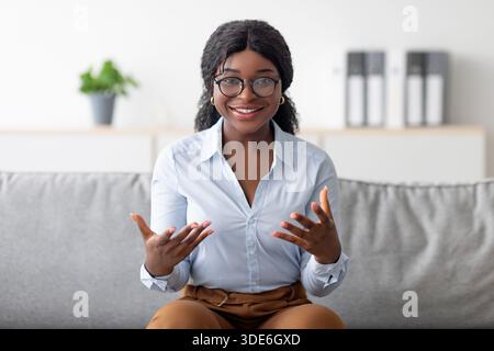 Porträt eines lächelnden jungen schwarzen Psychologen, der die Kamera anstischte und lächelte und auf der bequemen Couch im modernen Büro saß Stockfoto