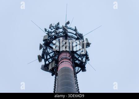 Mobilfunkturm mit zahlreichen Antennen, die Telekommunikationssignale gegen bewölkten Himmel übertragen Stockfoto