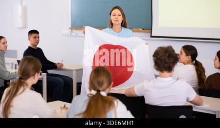 Der Lehrer erzählt den Schülern von Japan und hält eine japanische Flagge in der Hand. Stockfoto