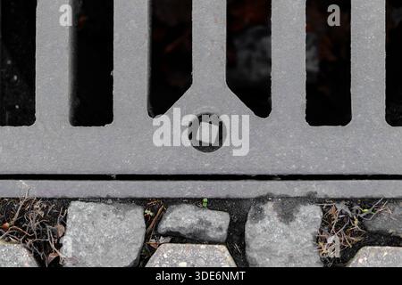 Nahaufnahme eines gusseisernen Abflussrostes und des umliegenden Pflasterpflasters Stockfoto