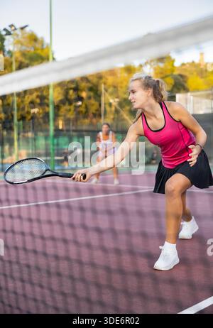 Positives Mädchen in Sportbekleidung beim Tennisspiel während des Trainings. Blick durch das Tennisnetz Stockfoto