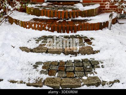 Steintreppen im Freien mit Ziegeln und Kopfsteinpflaster, teilweise mit frischem Winterschnee bedeckt, in der Nähe eines Gebäudeeingangs Stockfoto