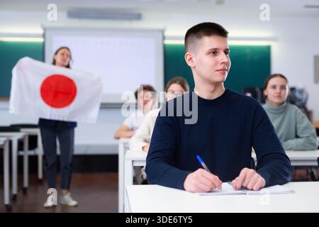 Der Lehrer erzählt den Schülern von Japan und hält eine japanische Flagge in der Hand. Stockfoto