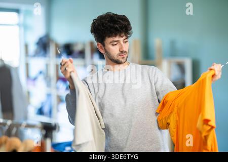 Ein junger Kerl, der ein T-Shirt im Bekleidungsgeschäft auswählt Stockfoto