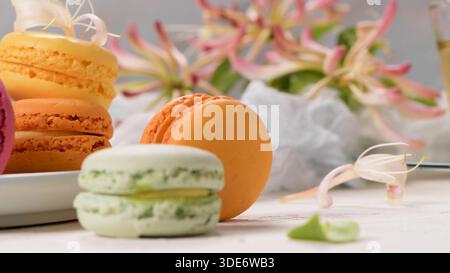 Köstliche Orangen- und Pistazienmakronen sind kunstvoll mit zarten rosa Geißblatt-Blüten angeordnet. Die sanfte, natürliche Beleuchtung unterstreicht das sanfte M Stockfoto