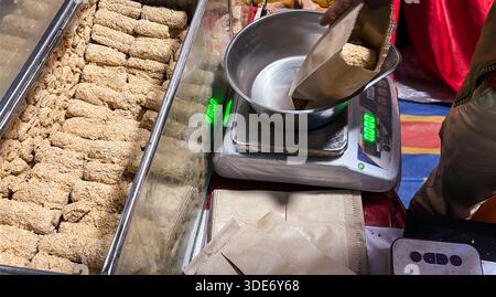 Traditionelle indische Süßigkeiten Sesambrüchig werden am Marktstand für den Einzelhandel gewogen Stockfoto