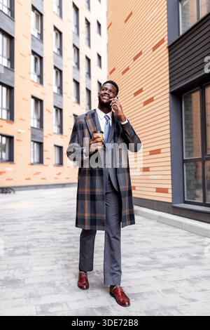 afroamerikanischer Geschäftsmann mit Kaffee zum Geschäftsanruf während der Pause, zu Fuß im Freien Stockfoto