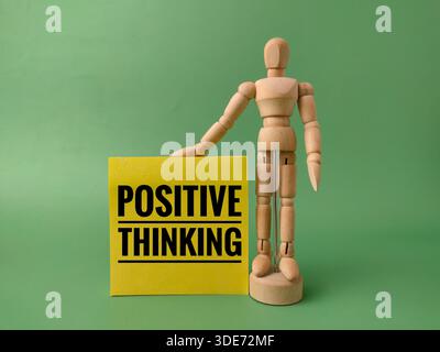 POSITIVES DENKEN geschrieben auf gelber Haftnotiz mit Holzfigur auf grünem Hintergrund. Stockfoto