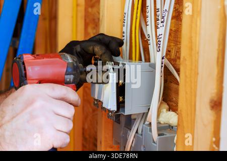 Ein Elektriker verwendet ein Elektrowerkzeug, um Leistungsschalter in der Wand des neu errichteten Hauses zu installieren Stockfoto