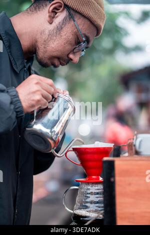 Nahaufnahme eines Barista, der mit einem Wasserkocher aus Edelstahl Wasser über Kaffeesatz in einem roten Tropfer gießt. Stockfoto