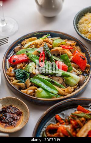 Gebratene Reiskuchen mit gemischtem Gemüse, serviert auf einem gut gedeckten Esstisch, begleitet von einer Schüssel Reis und Chili-Öl. Stockfoto